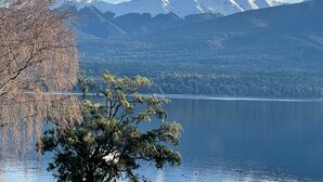 A serene lake with a tree in the foreground and snow-capped mountains in the background. - Lakewood Lofts (Te Anau)
