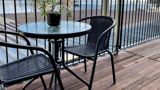 A wooden deck with a glass table and two wicker chairs, overlooking a calm lake and distant mountains. - Lakewood Lofts (Te Anau)