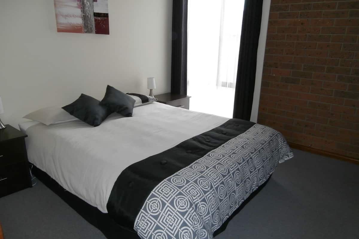 A modern bedroom with a large bed, a nightstand, a lamp, and a window with curtains.