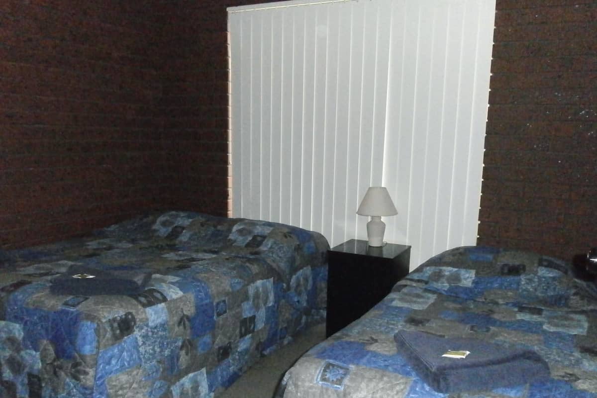 A hotel room with two beds, a nightstand with a lamp, and a window with blinds.