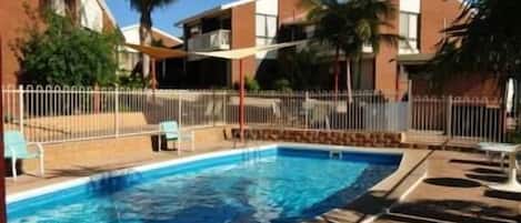 Una piscina al aire libre, sillones reclinables de piscina