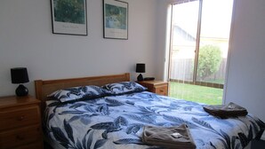 Ein Schlafzimmer mit einem Bett, zwei Nachttischen, einem Holz-Kopfteil und zwei gerahmten Kunstwerken an der Wand.