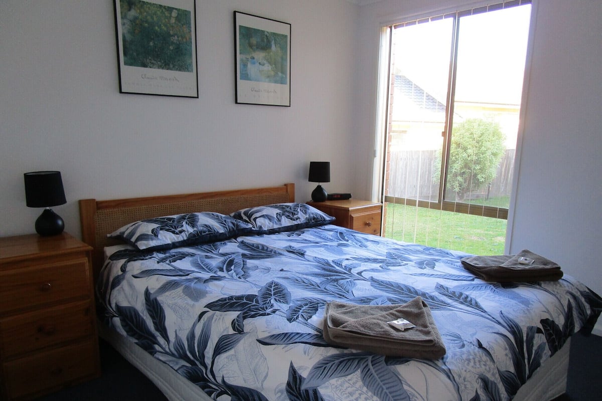 A bedroom with a bed, two nightstands, a wooden headboard, and two framed artworks on the wall.