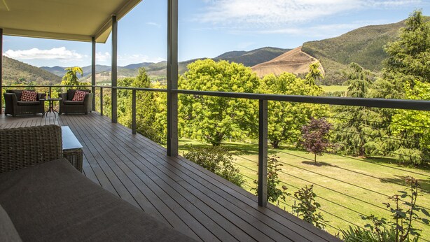 A wooden deck with wicker furniture and a view of a lush landscape.