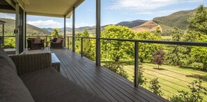 A wooden deck with wicker furniture and a view of a lush landscape. - Abby's Cottages (Wandiligong)