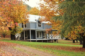 A two-story house with a porch, surrounded by trees with autumn leaves. - Abby's Cottages (Wandiligong)
