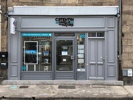 Une devanture de magasin avec une enseigne indiquant « COTENTIN, UN LIEU UNIQUE » et une vitrine où est affichée une affiche.