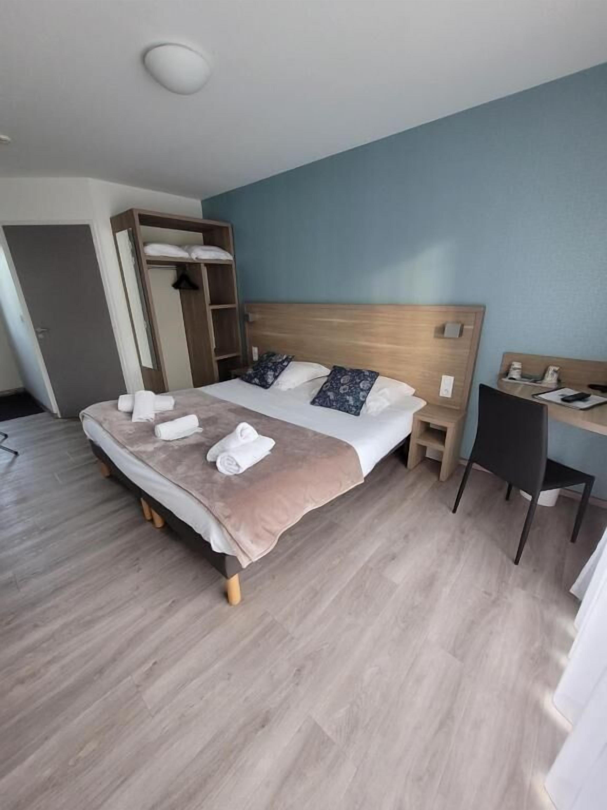 A neatly made bed with pillows, a bedside table, a desk with a chair, and a wardrobe.
