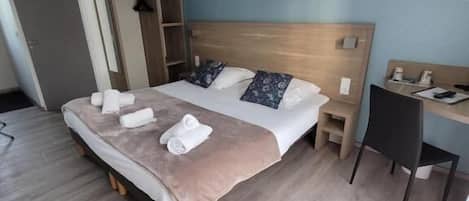 Una cama bien hecha con almohadas, una mesita de noche, un escritorio con una silla y un armario.