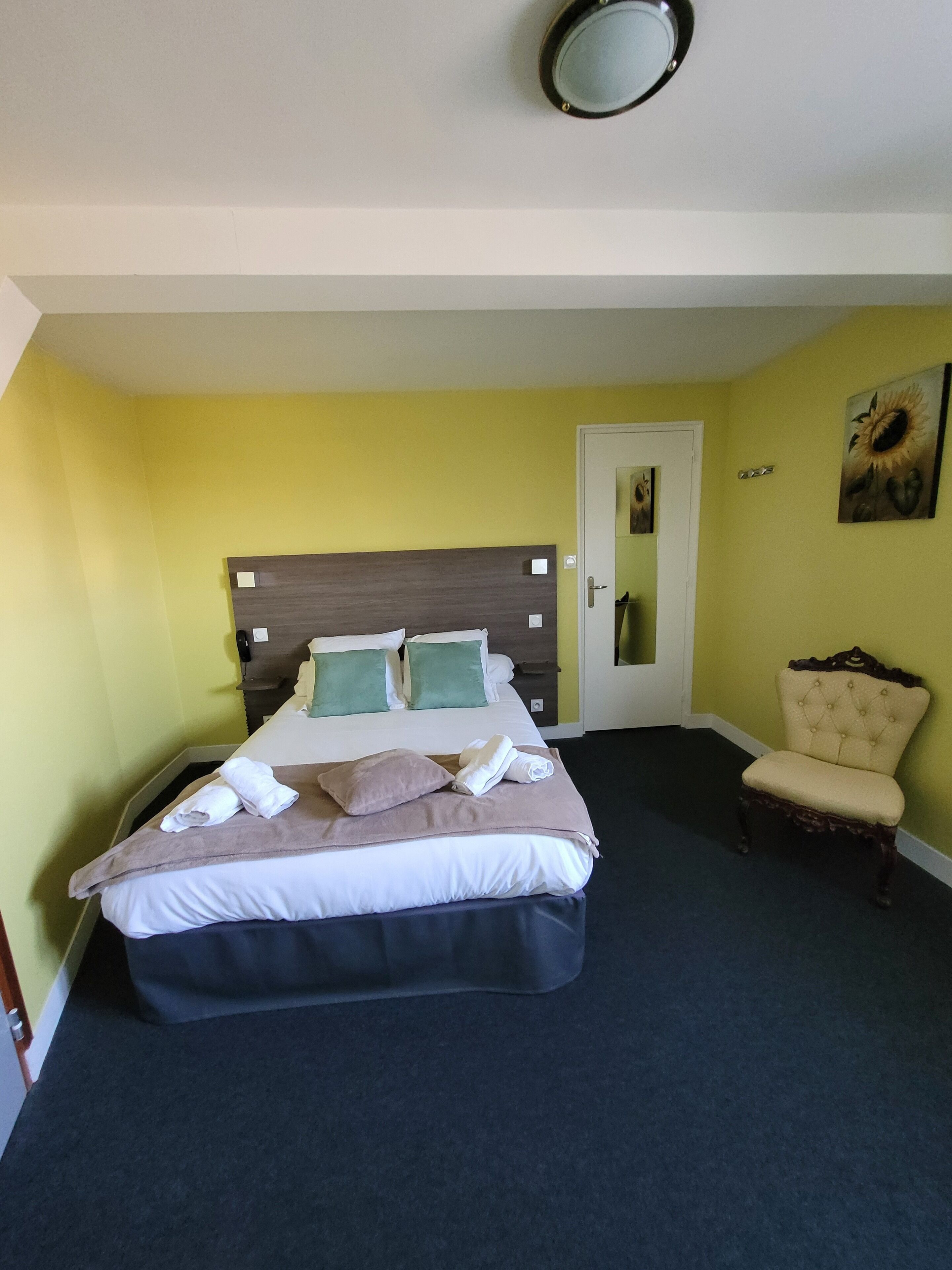 A neatly made bed with pillows and a blanket, a chair, and a door with a mirror.