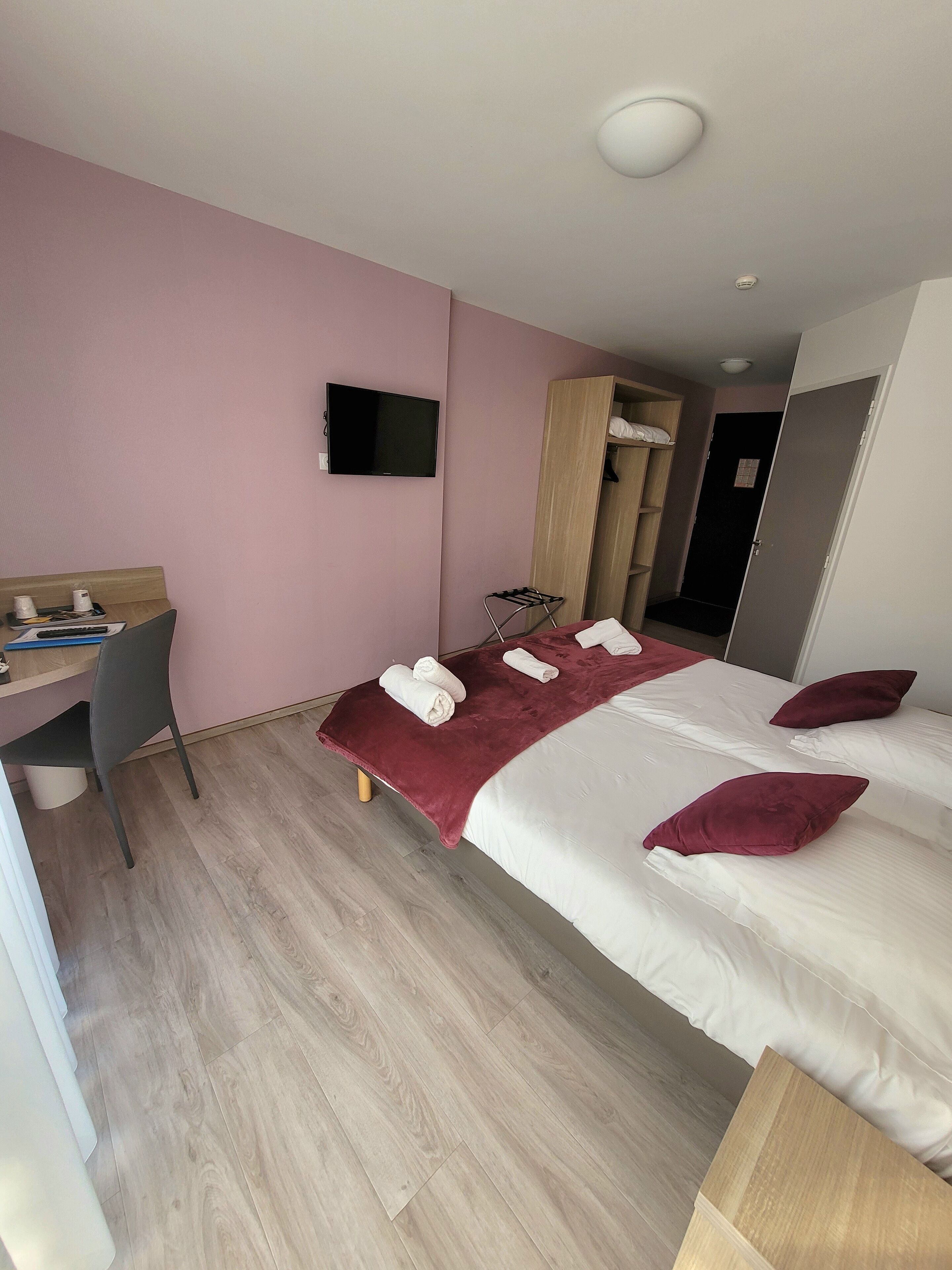 A hotel room with a bed, a desk, a chair, a TV, and a wardrobe.