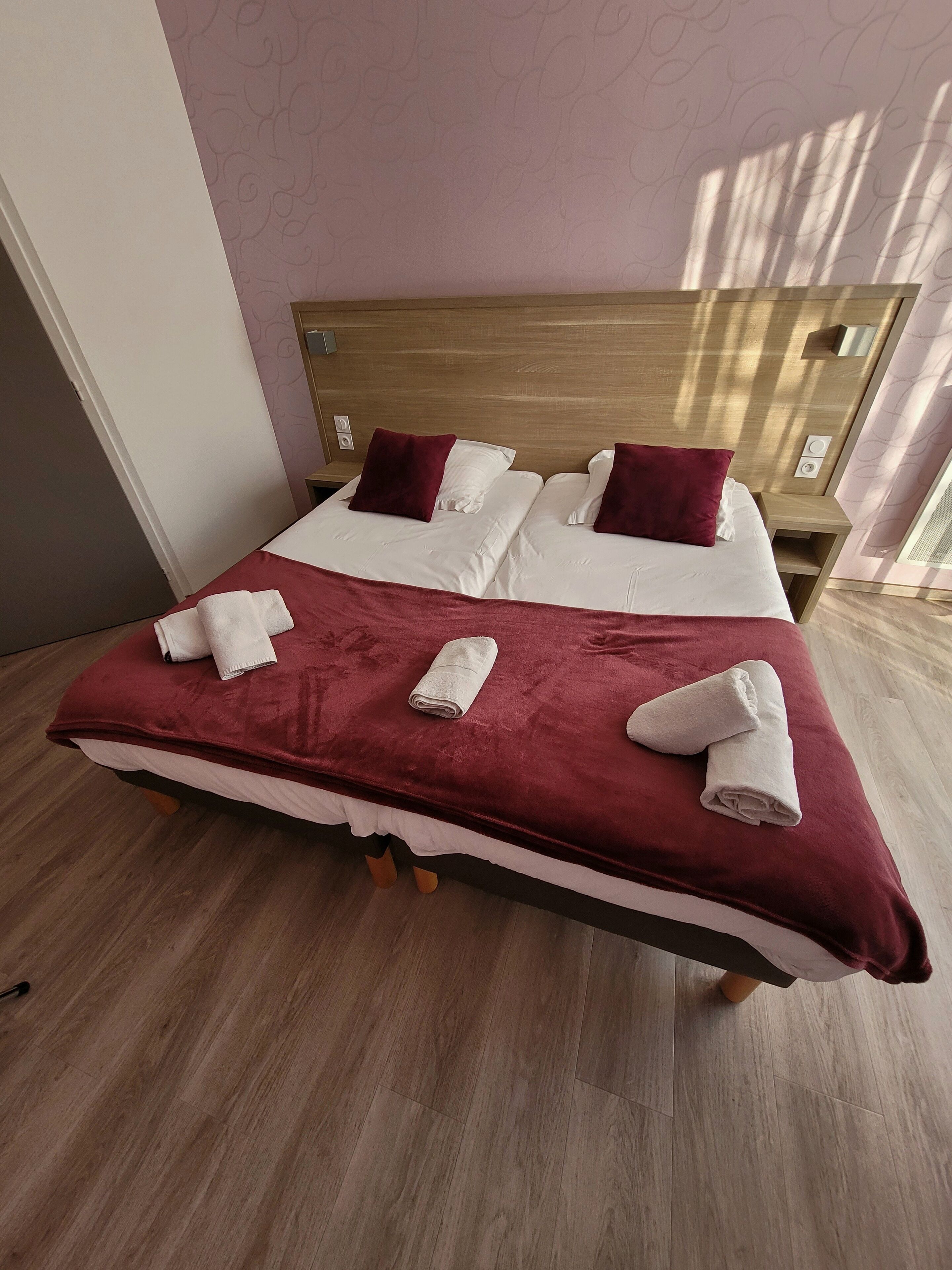 A neatly made bed with white and maroon linens, a wooden headboard, and a red throw blanket.