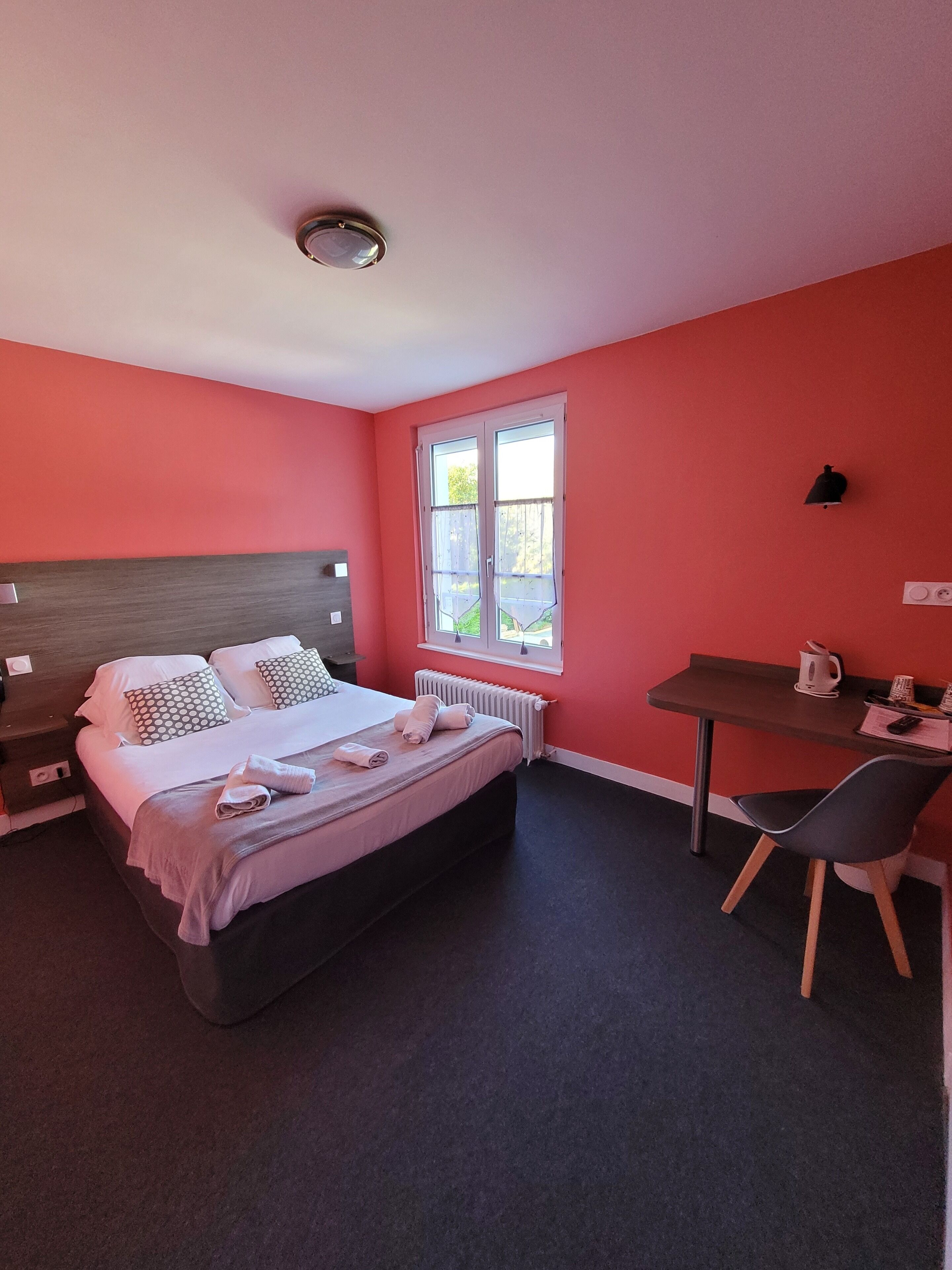 Una habitación de hotel con una cama, un escritorio, una silla, un ventanal y un radiador.