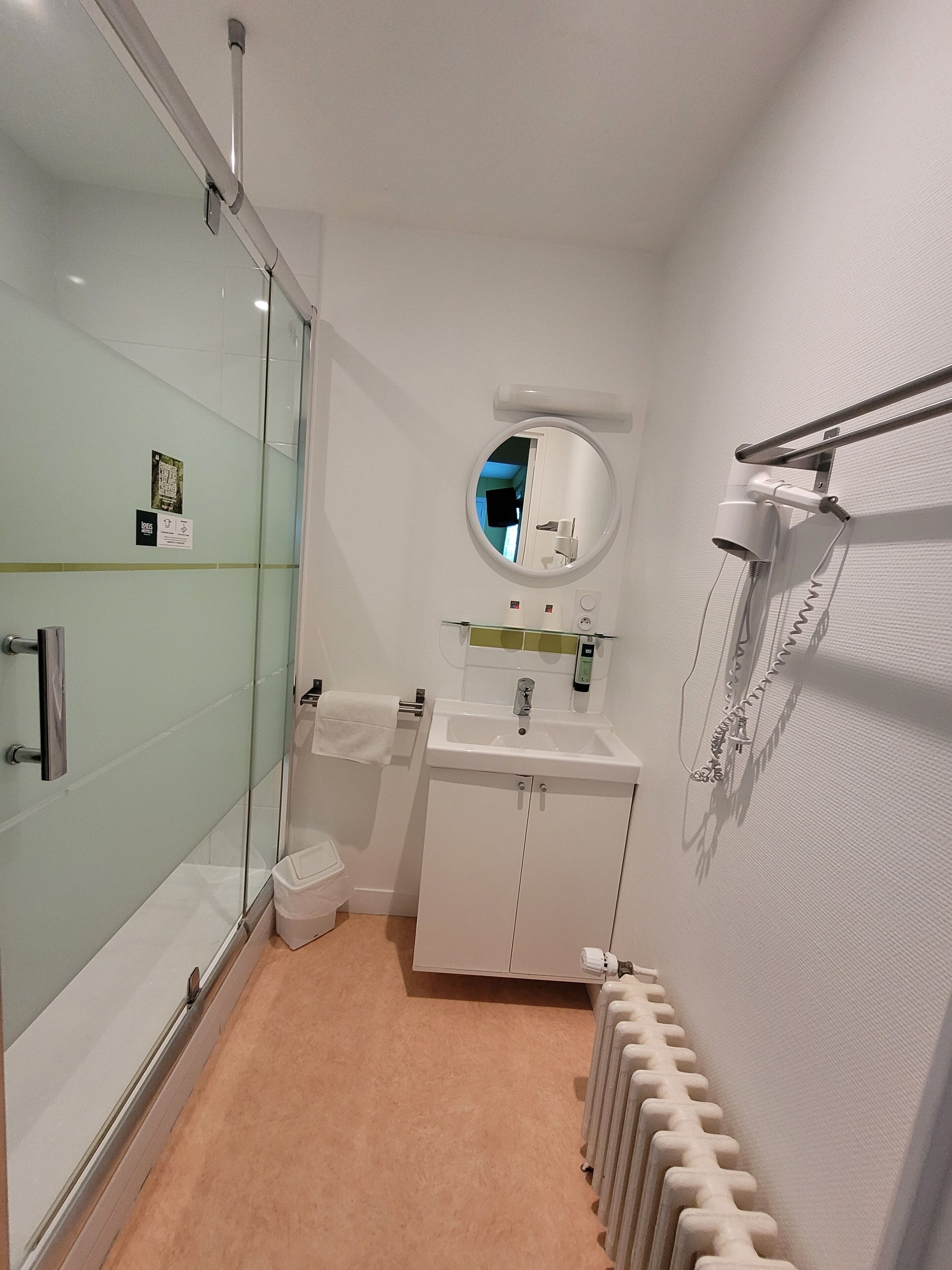 Un baño con cabina de ducha de vidrio, un lavabo con espejo y un radiador en la pared.