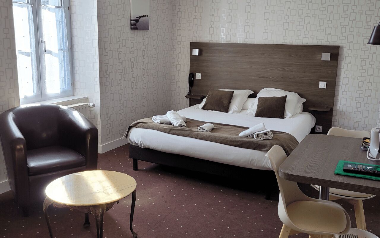 Una habitació d'hotel amb un llit, una cadira, una taula i una finestra.