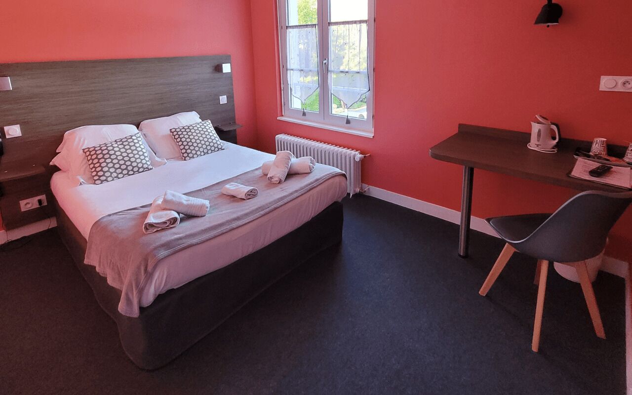 A hotel room with a bed, a desk, a chair, a radiator, and a window.