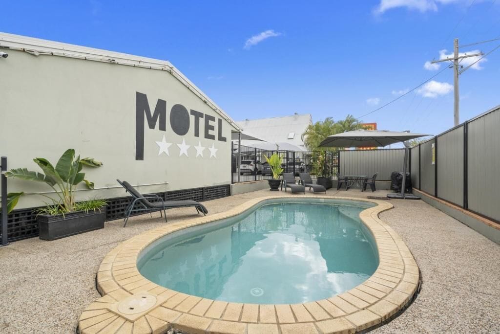 A motel with a swimming pool, lounge chairs, and a patio area.