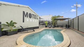 A motel with a swimming pool, lounge chairs, and a patio area.