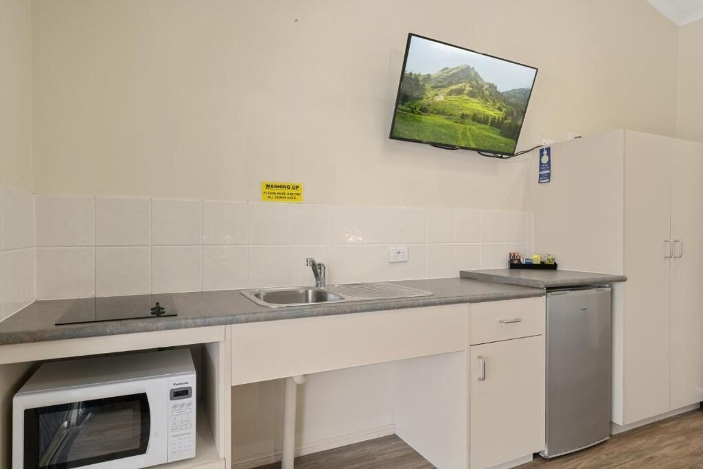 A kitchen with a microwave, sink, and a flat-screen TV mounted on the wall.