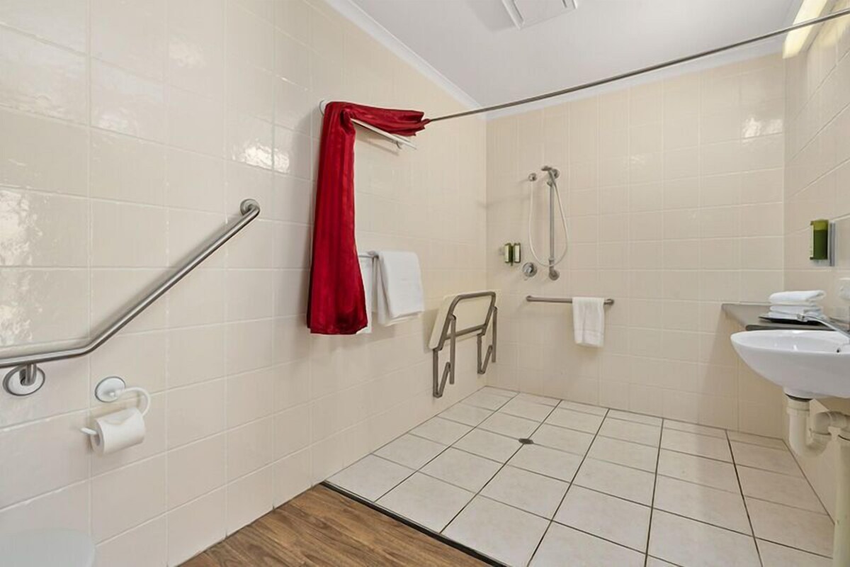 Un bagno con piastrelle bianche, un asciugamano rosso, una doccia, un lavandino e una barra di sostegno.