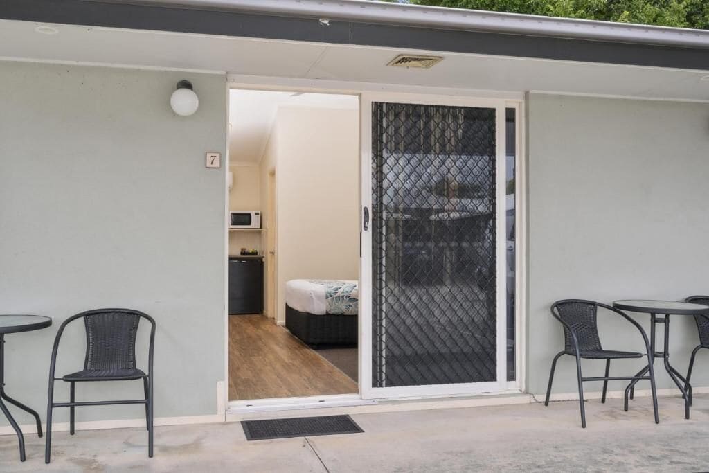 A room with a bed, a desk, and a chair. There is a sliding door with a mesh screen.