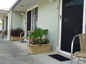 A covered outdoor area with a planter box containing flowers and a wicker chair. - Caboolture Central Motor Inn (Caboolture)
