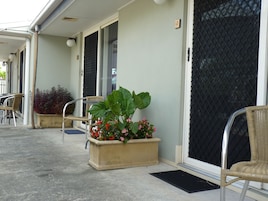 Un espacio al aire libre techado con una jardinera con flores y una silla de mimbre.