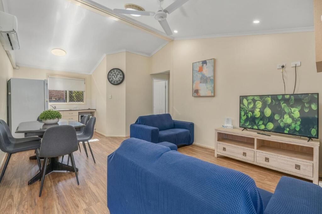 A modern living room with a dining area, a flat-screen TV, and a ceiling fan.