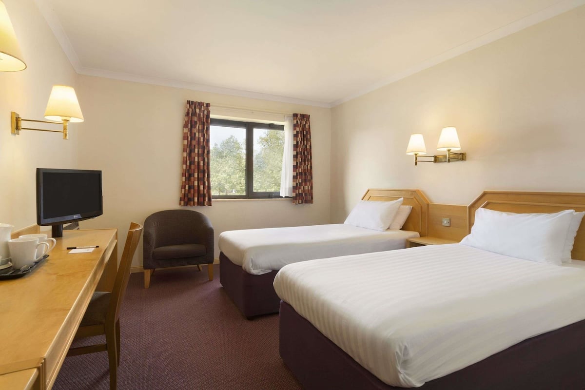 A hotel room with two beds, a desk with a computer, a chair, and a TV.