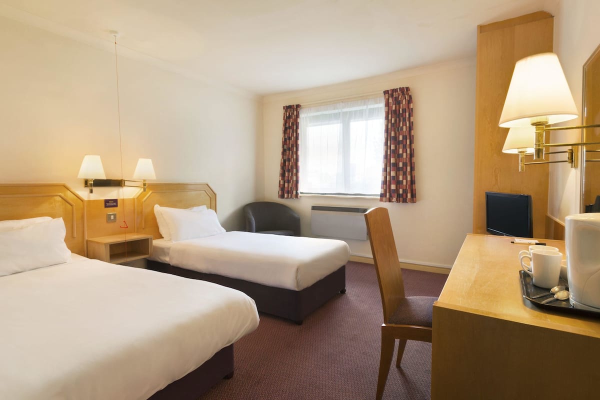A hotel room with two single beds, a desk with a chair, a coffee maker, and a television.