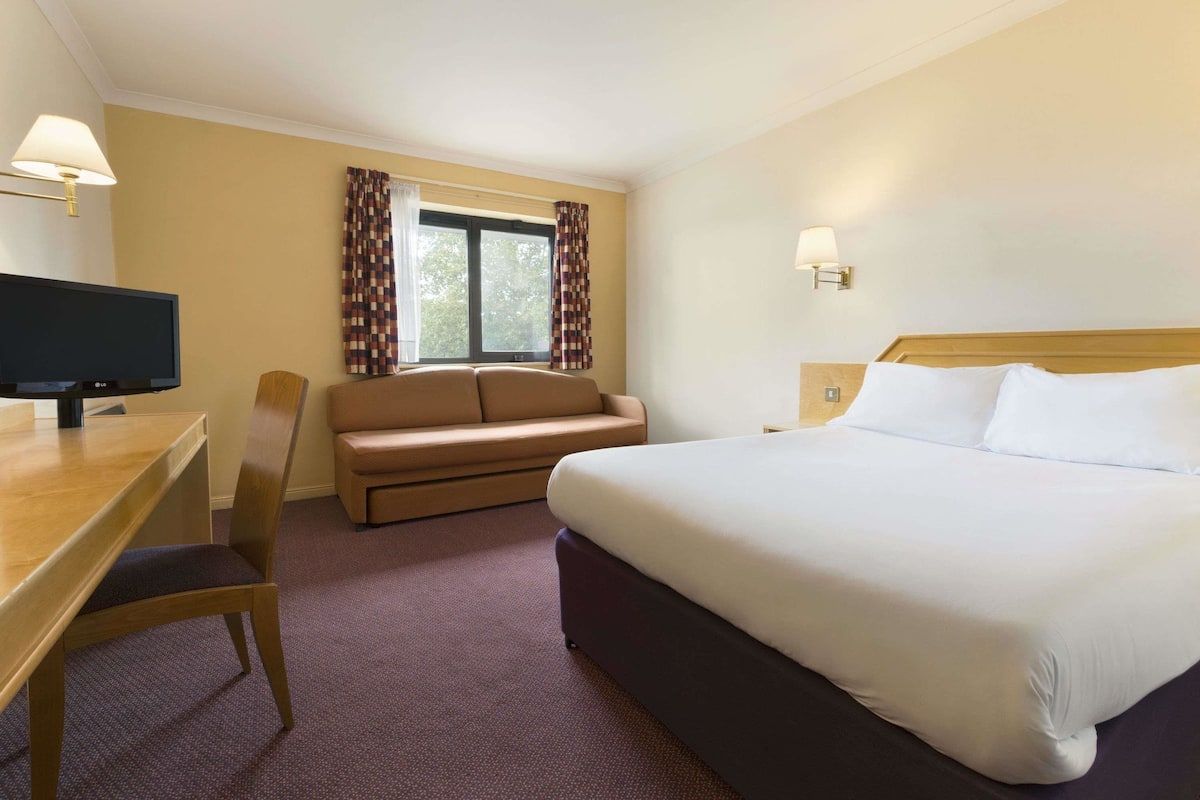 A hotel room with a bed, a sofa, a desk, and a television.