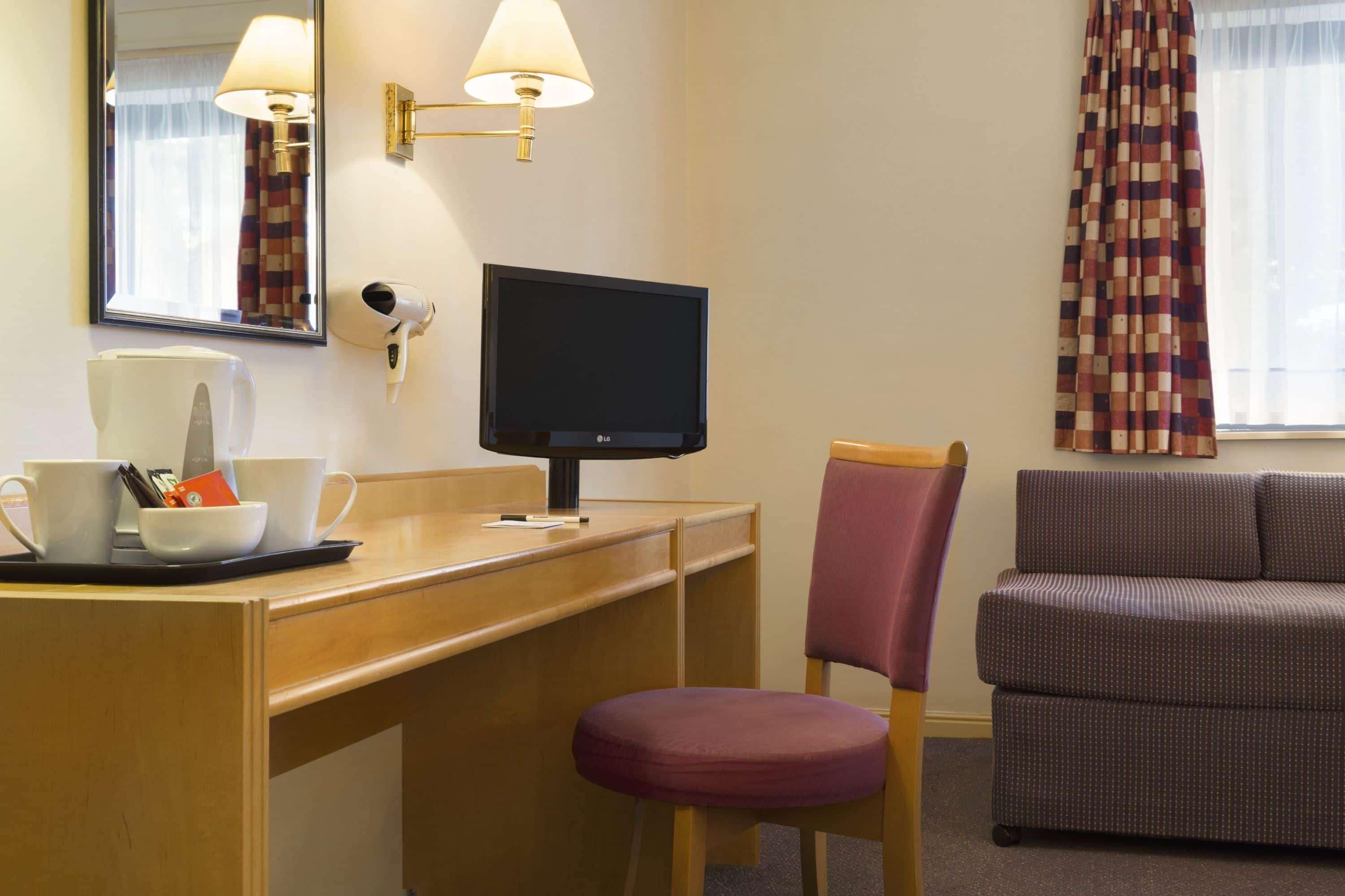 Een hotelkamer met een bureau, een televisie, een stoel en een bank.