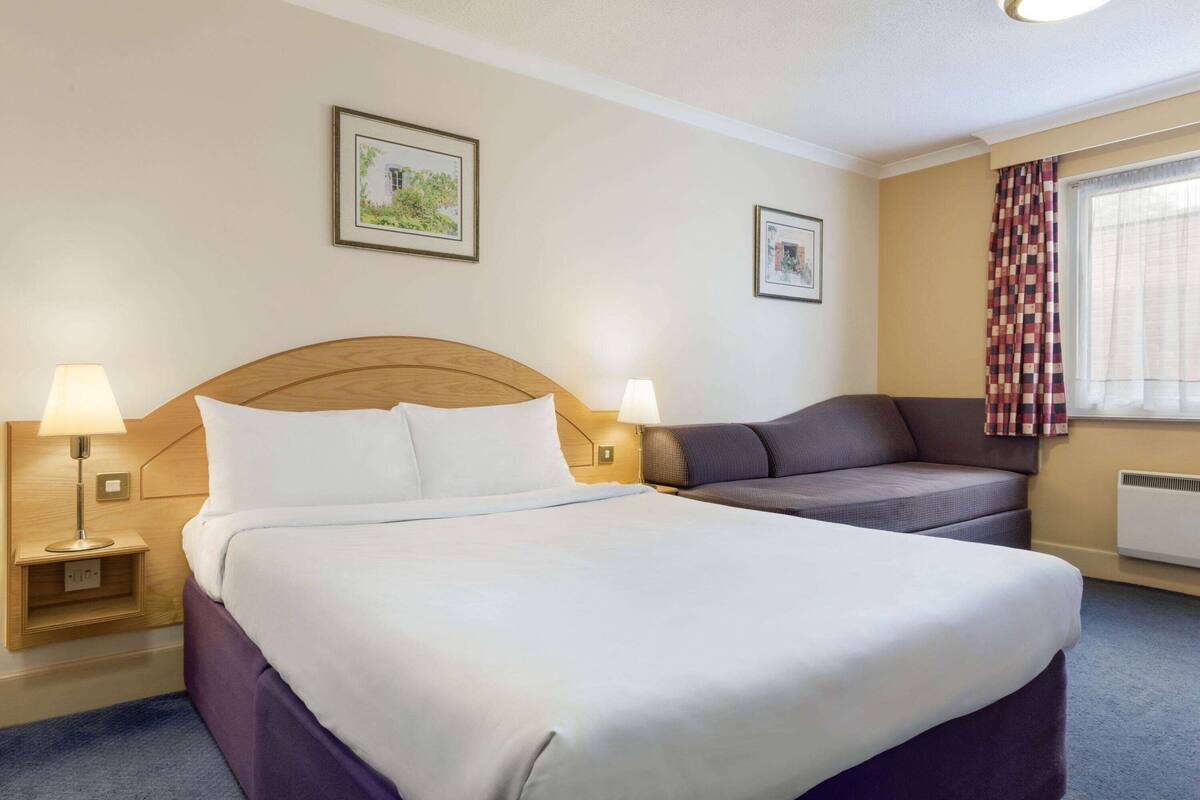 Ett hotellrum med en stor säng, en soffa, två vägglampor och två inramade tavlor på väggarna.