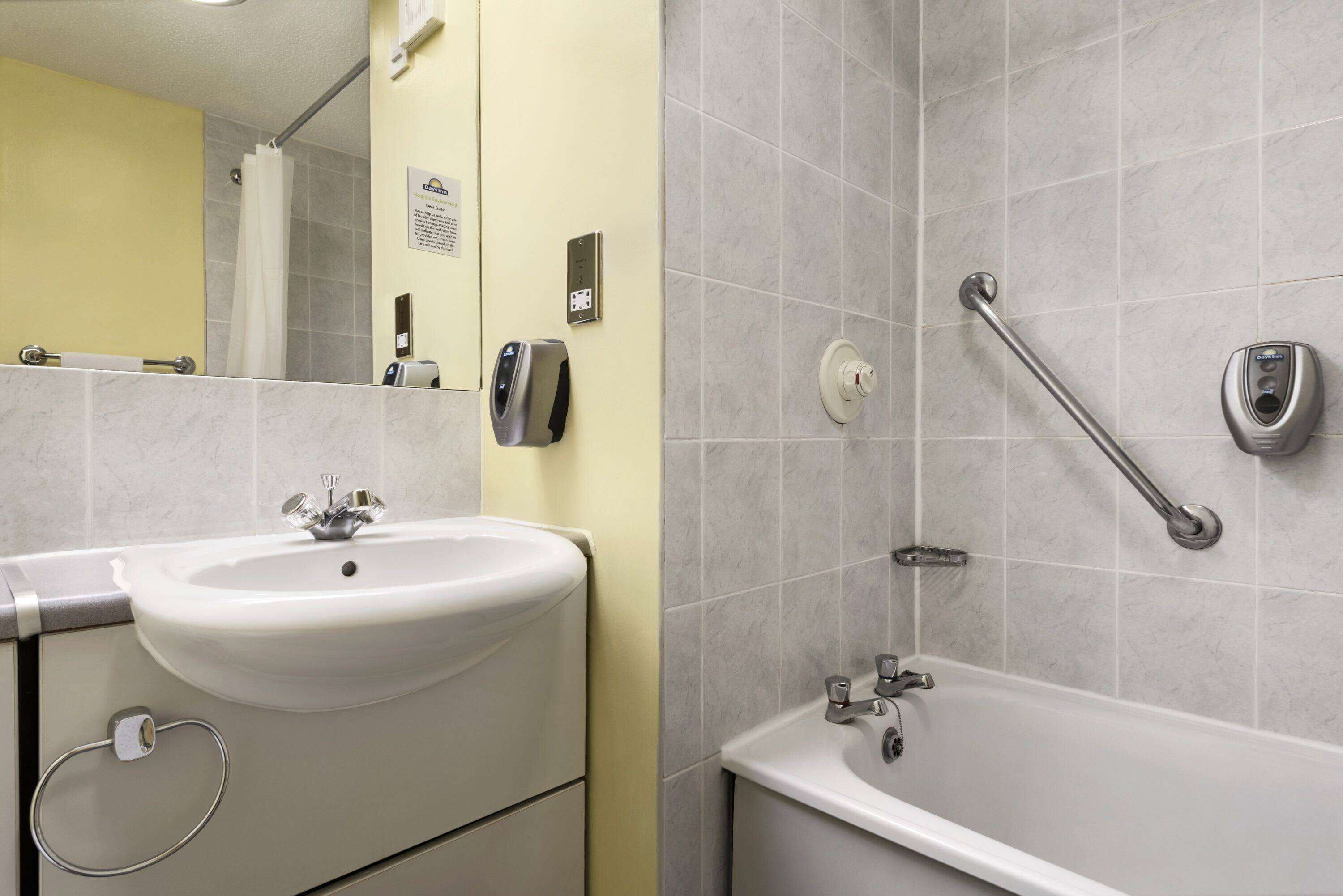 Baño con lavabo, espejo, ducha y barras de apoyo.
