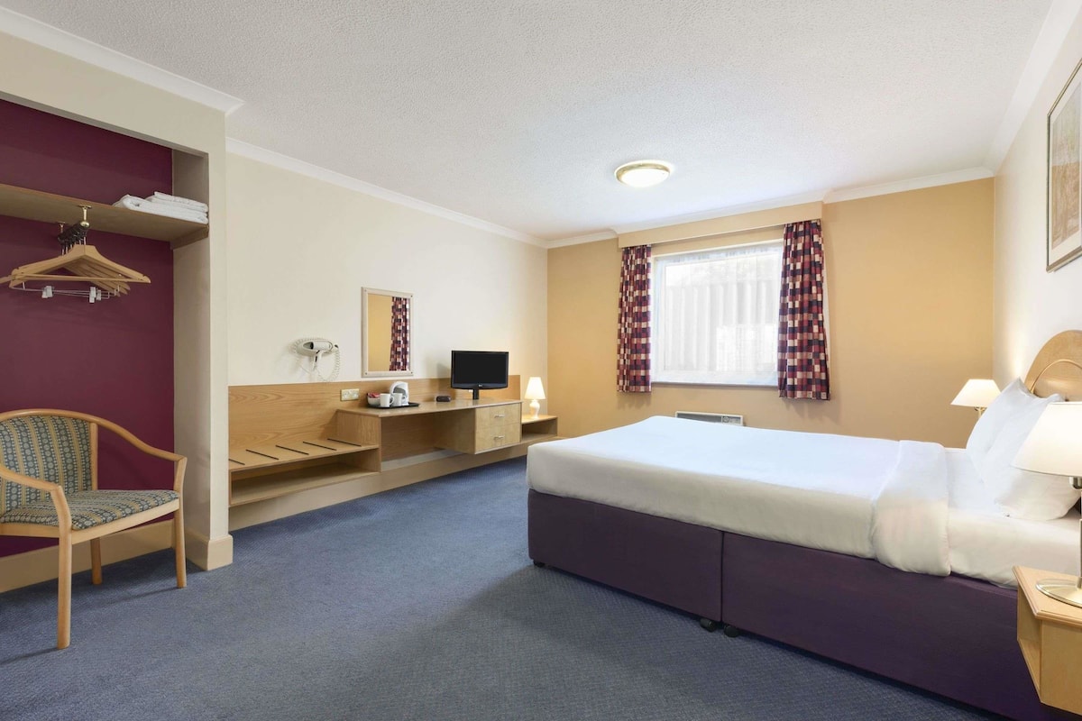 Ett hotellrum med en säng, ett skrivbord, en stol och ett fönster med gardiner.