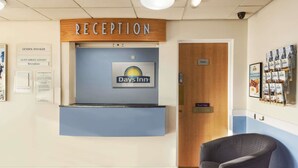 A reception area with a sign for Days Inn, a reception desk, and a guest service contact notice. - Days Inn by Wyndham Watford Gap (Northampton)