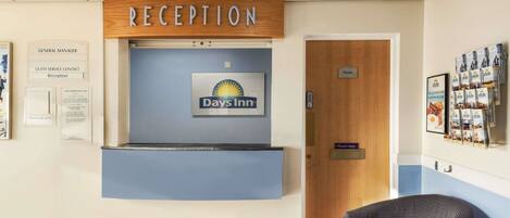 Un espace d’accueil avec une enseigne Days Inn, un comptoir de réception et un avis indiquant les coordonnées du service d’assistance à la clientèle.