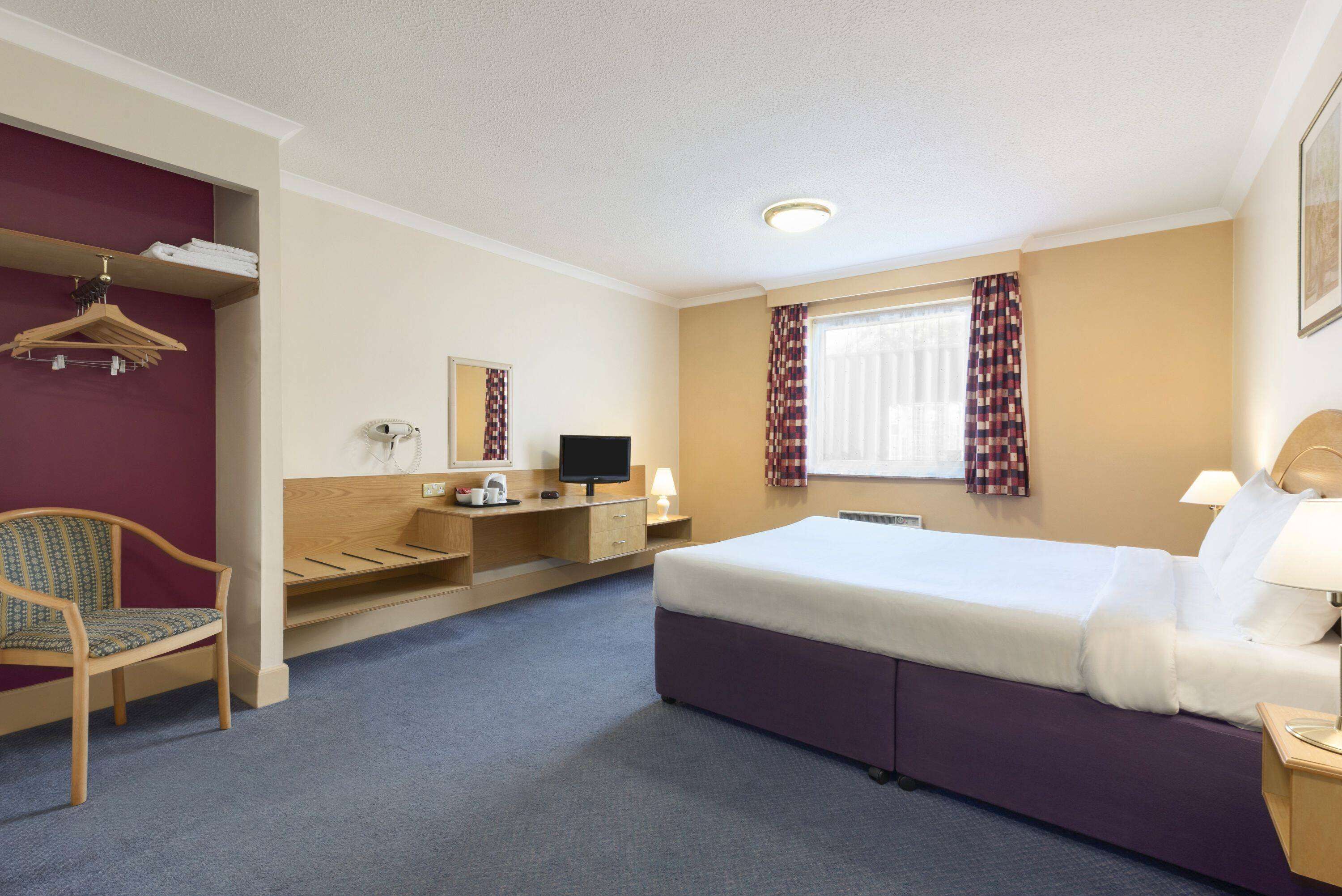 Ein Hotelzimmer mit Bett, Schreibtisch, Stuhl und Kleiderschrank.