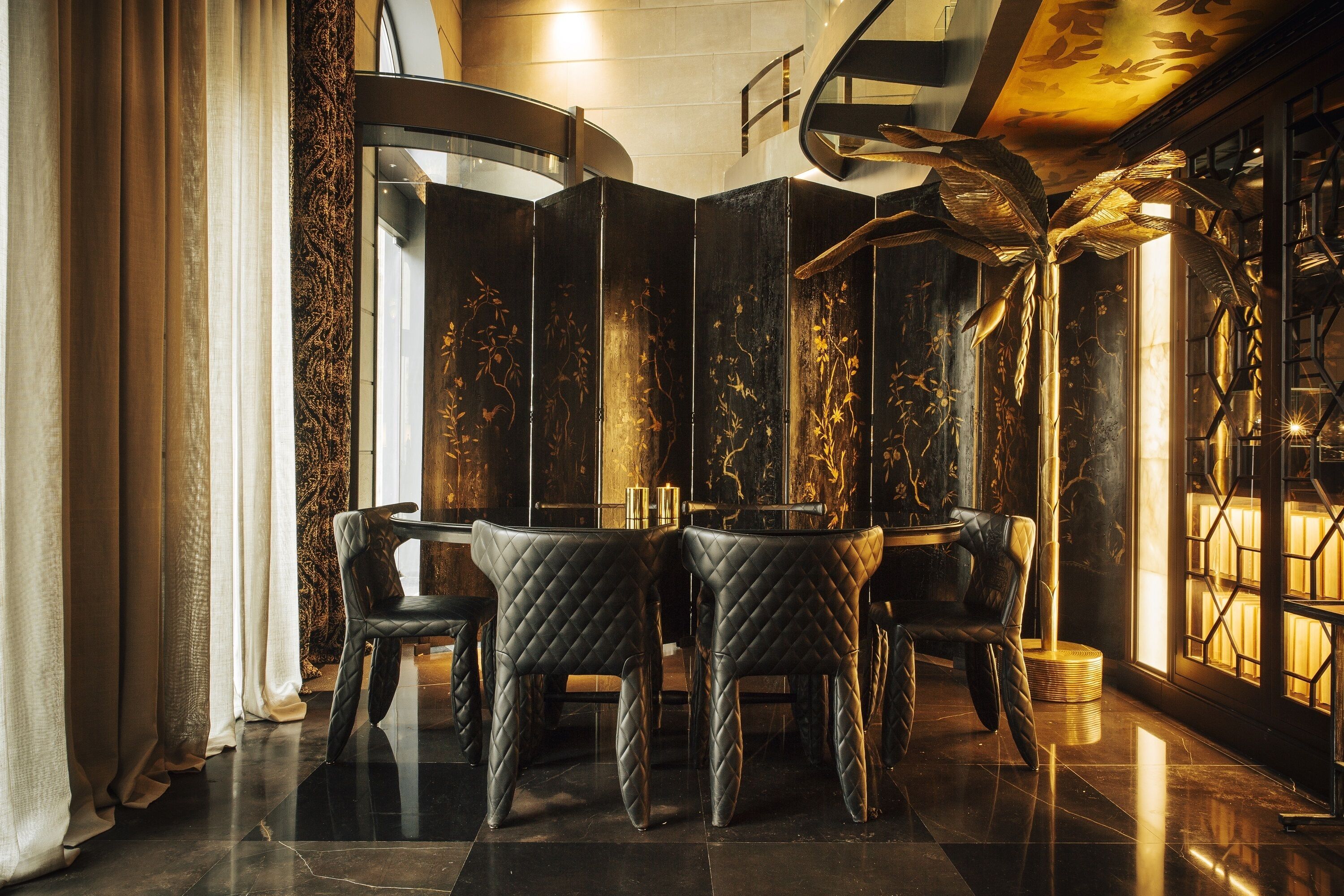 A luxurious interior with a round table and four chairs, a decorative plant, and a large window with a view.