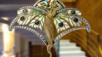 A detailed brooch with a butterfly design, featuring gemstones and a pearl pendant.
