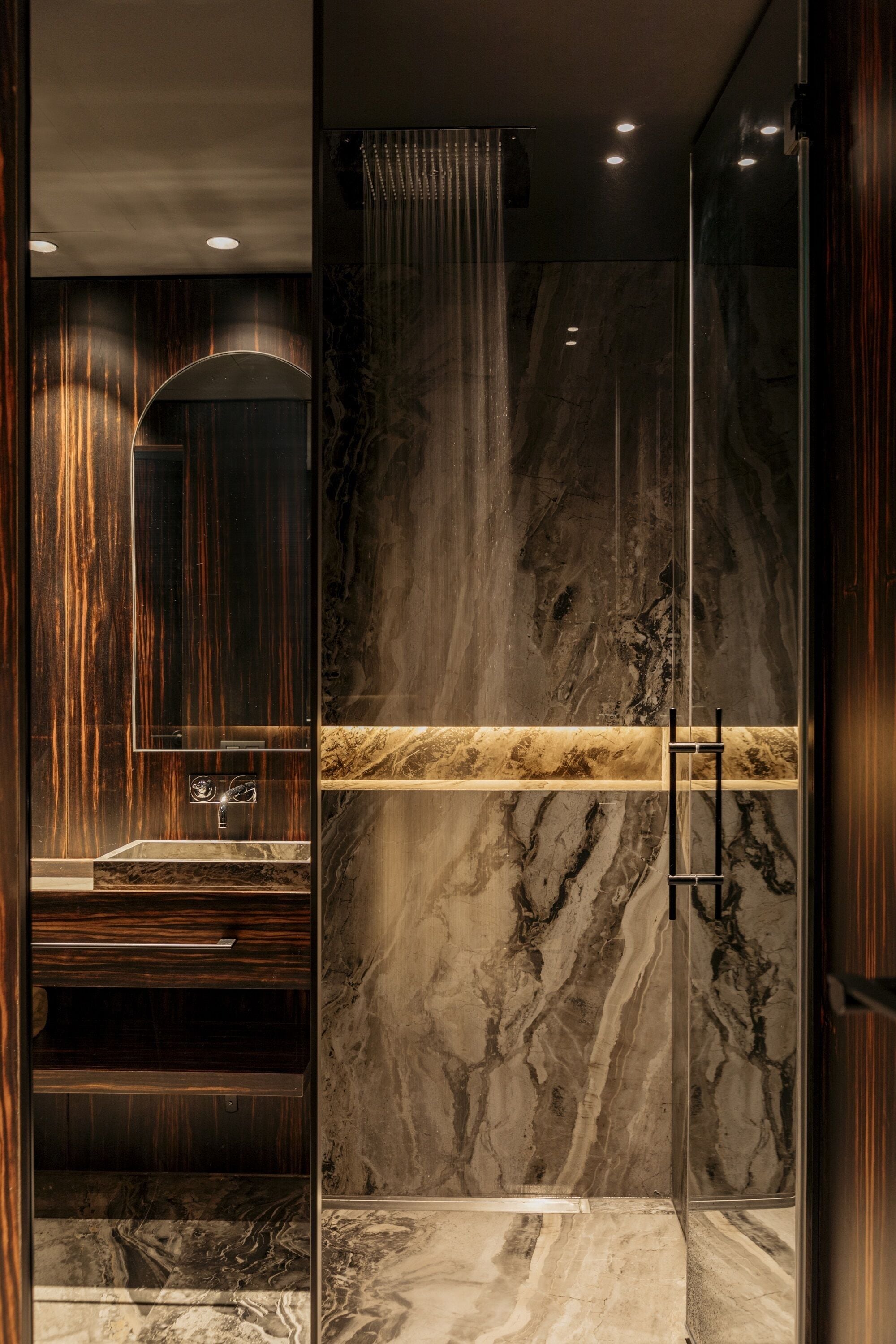 A modern bathroom with a marble vanity, a large mirror, and a glass shower enclosure.