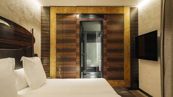 Una habitació d'hotel moderna amb un llit gran, un armari de fusta, una porta de vidre que condueix a un bany i un televisor penjat.