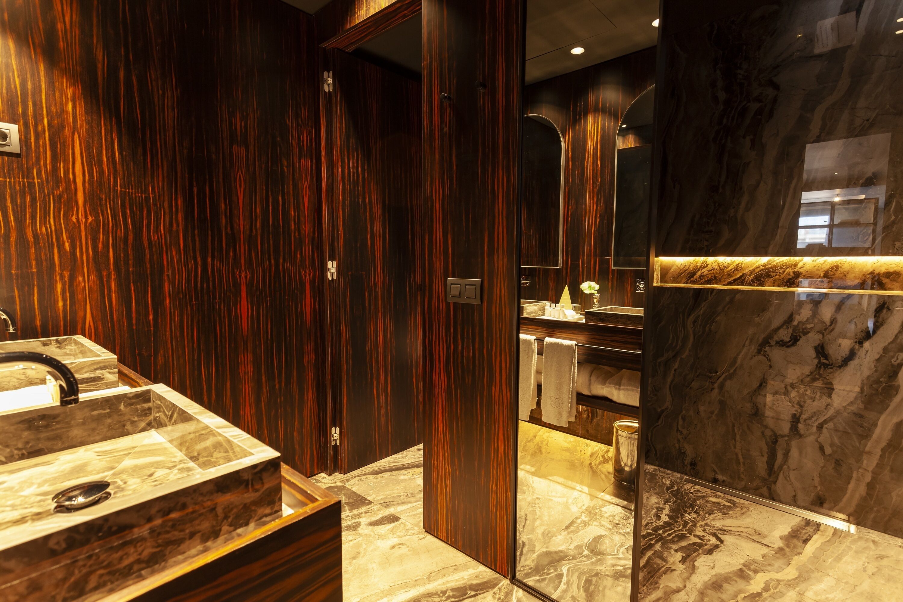 A modern bathroom with a marble sink, wooden paneling, and a large mirror.