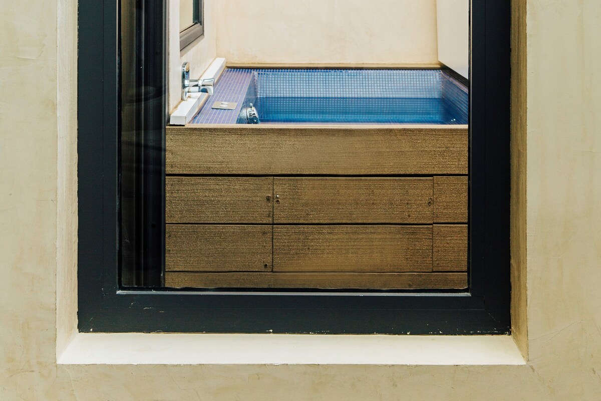 Ein kleiner, abgeschlossener Raum mit Fenster, einer hölzernen Bank und Fliesenboden.