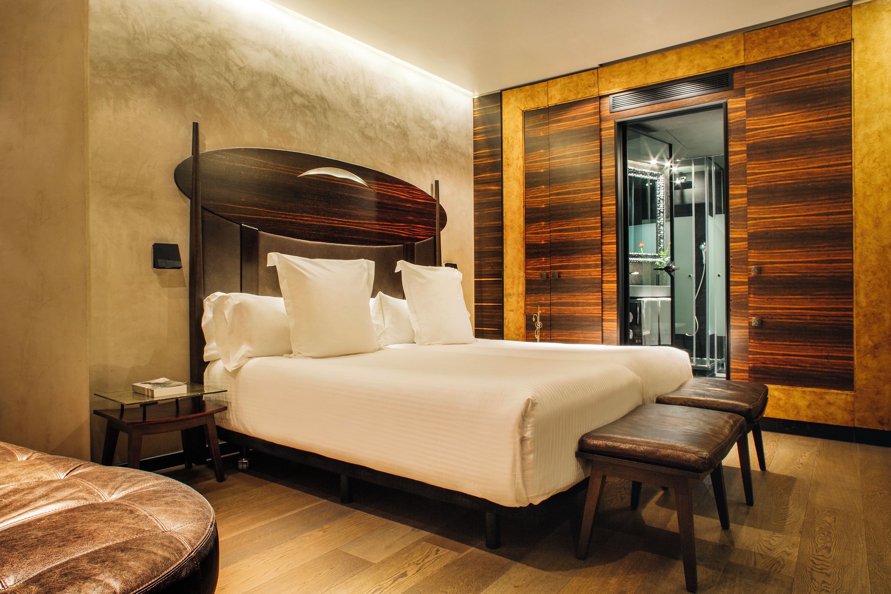 A bedroom with a large bed, a wooden headboard, a glass table, and a bench.