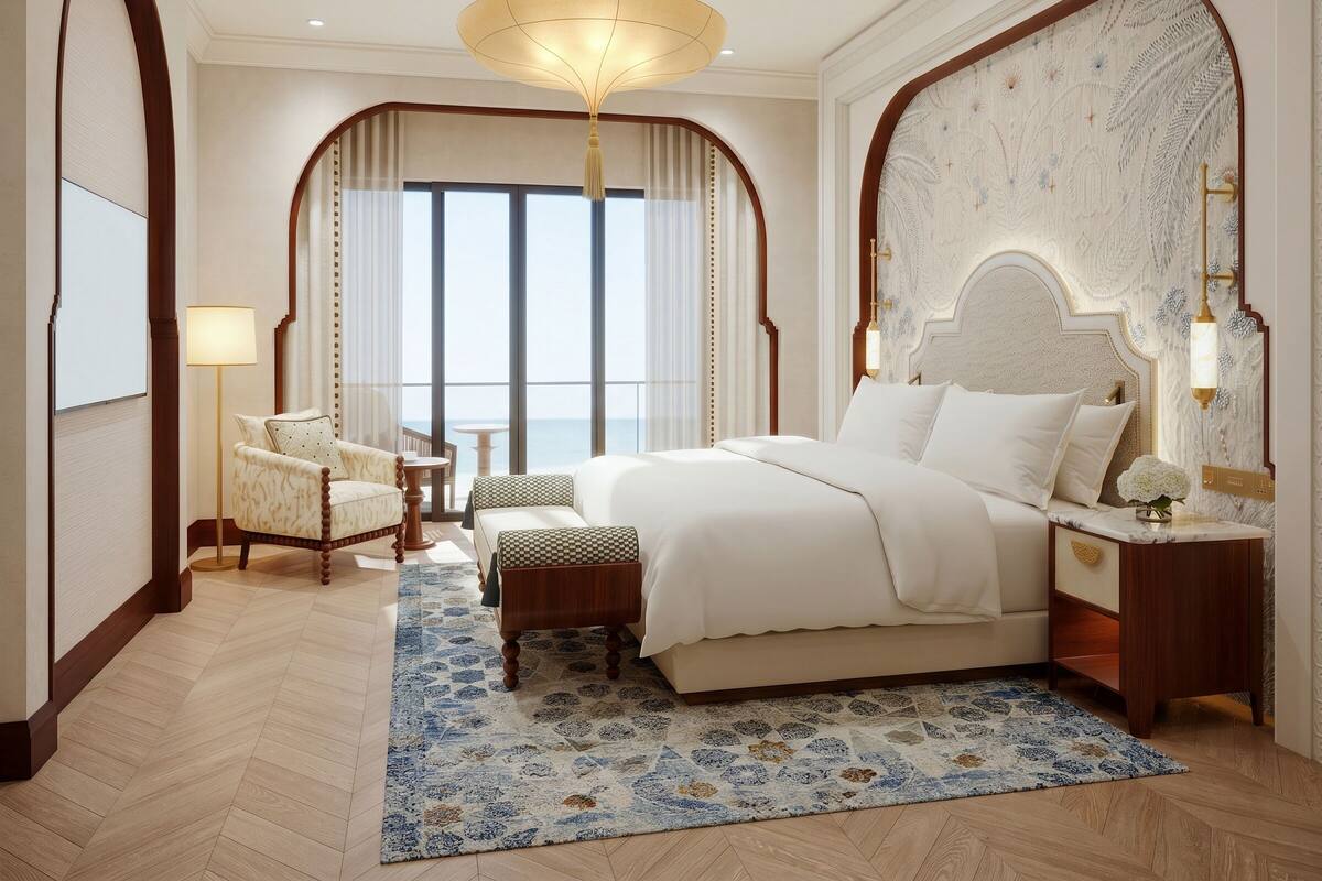Une chambre spacieuse avec un grand lit, un coin salon comprenant un fauteuil et une table, et une vue sur la mer grâce à de grandes fenêtres.