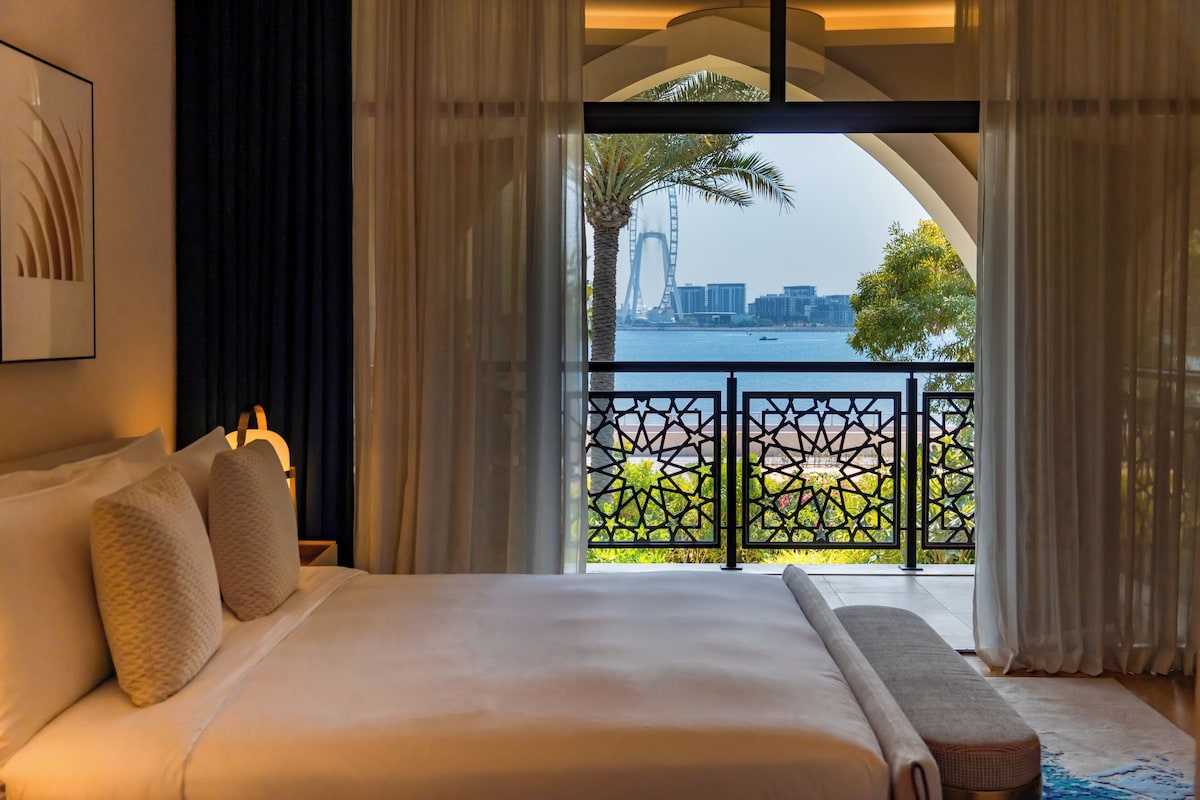 Habitación de hotel con una cama grande, vistas a la ciudad y un balcón con barandilla decorativa.
