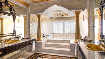Features a grand sink, ornate columns, and a large mirror, with a marble staircase leading to a shower area.