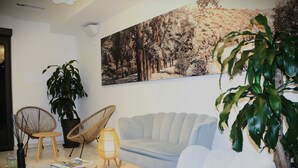 Una sala de estar con un sofá azul claro, dos sillones de mimbre, una mesa de centro de vidrio, una planta grande en maceta y un cuadro colgado en la pared.