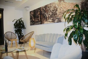 Un salon avec un canapé bleu clair, deux fauteuils en osier, une table basse en verre, une grande plante en pot et un tableau accroché au mur.